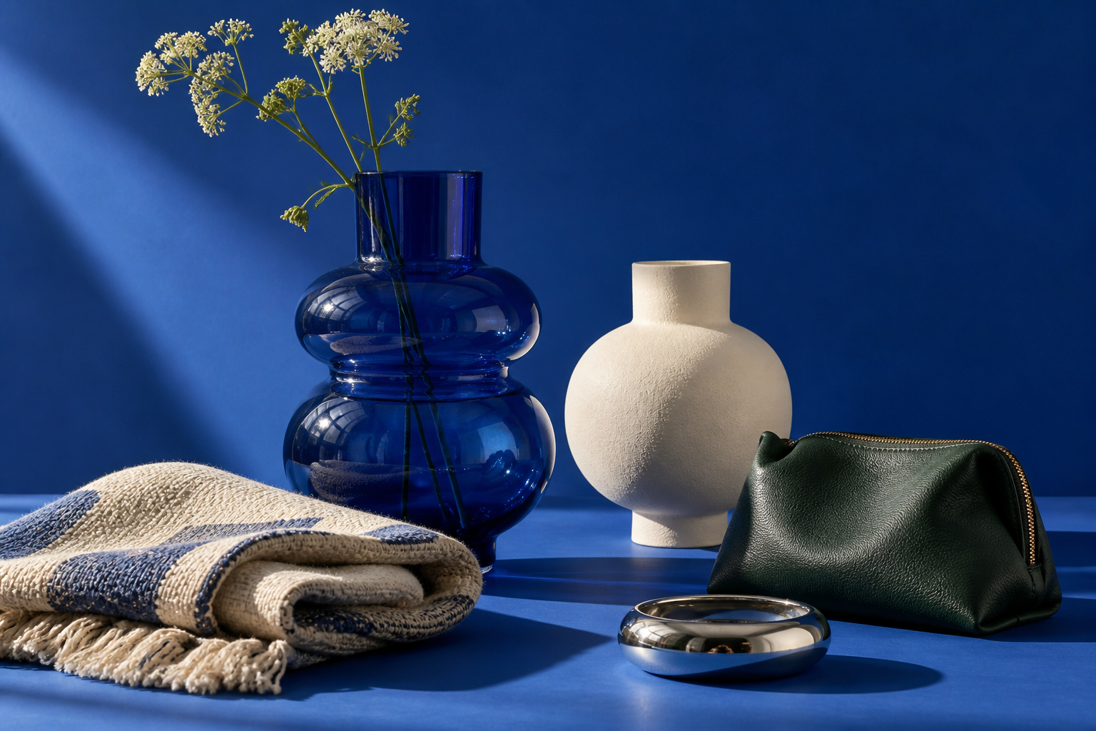 A still life of vases, a throw and everyday accessories against a blue backdrop